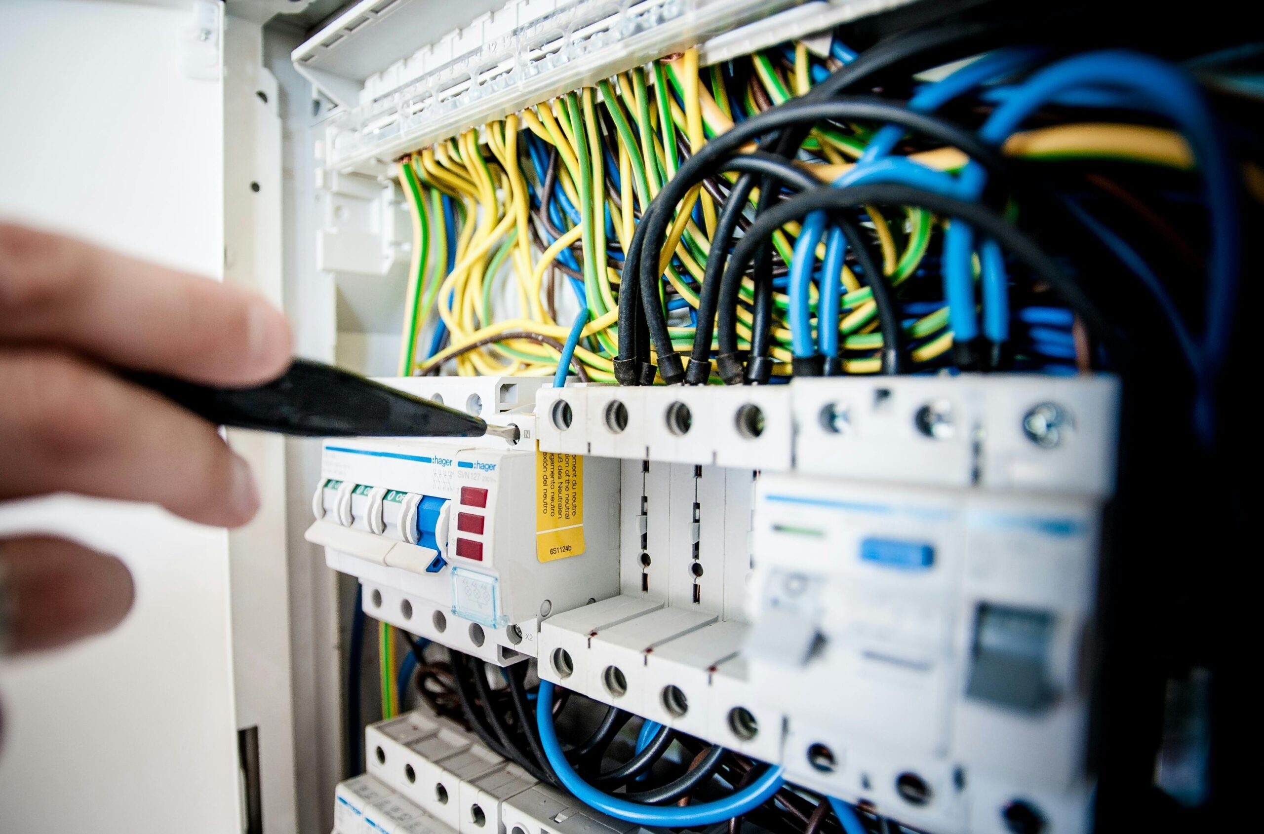 Hand of electrician working on a circuit breaker panel with colorful wires, ensuring safe electrical connections.